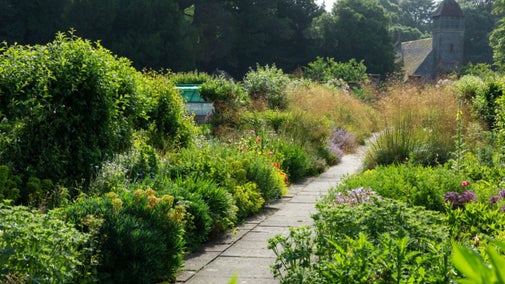 Summer borders with a flag stoned path through the middle of Hinton Ampner's walled garden, with church in the background.
